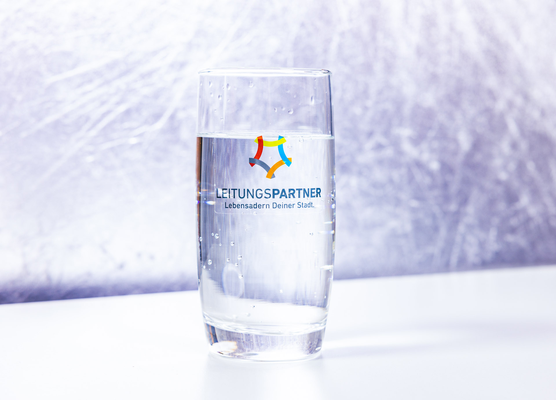 Glas gefüllt mit Wasser mit Aufschrift und Logo der Leitungspartner GmbH